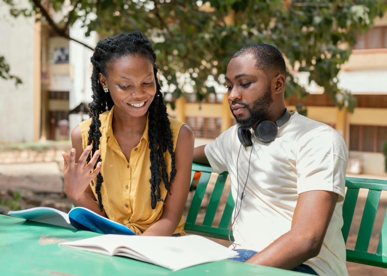 A student explaining her work to another on a campus bench